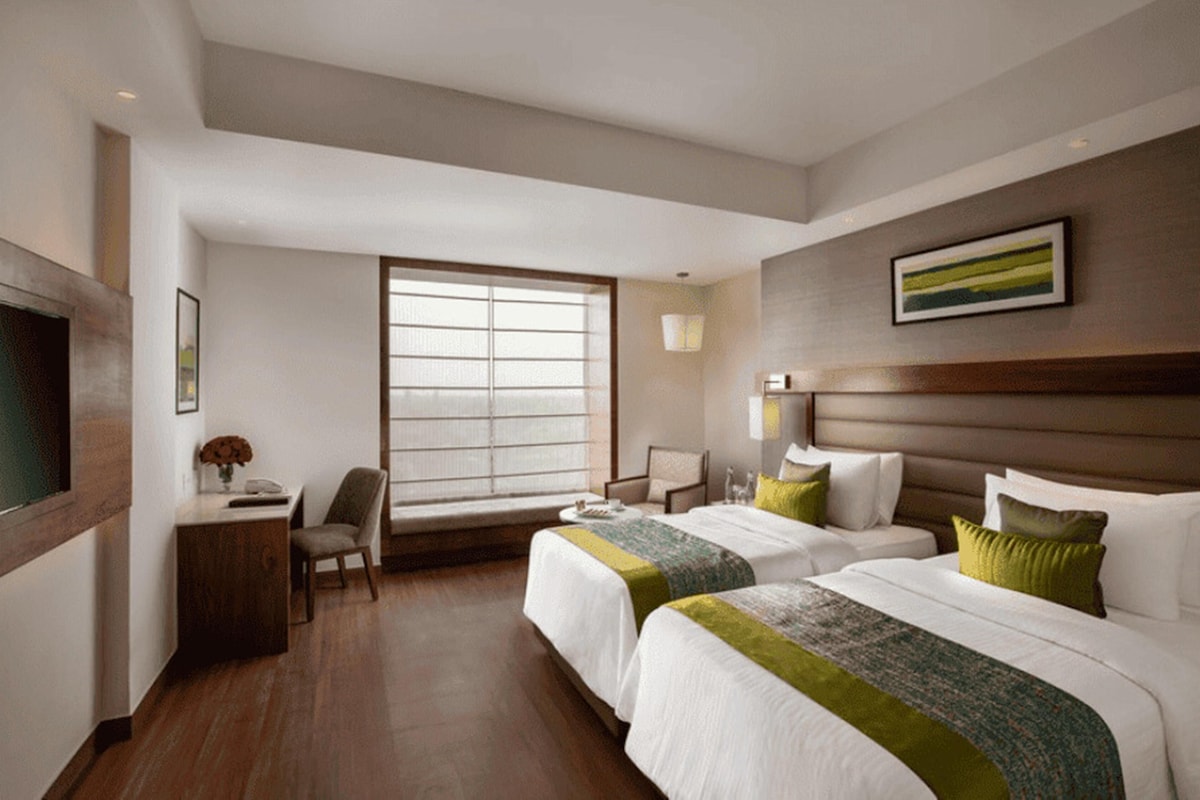 Une chambre d’hôtel avec deux lits, un bureau, une chaise, une fenêtre et un tableau encadré au mur.