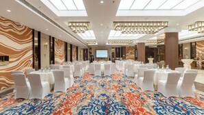 Un salón de conferencias con mesas redondas, sillas blancas y una pantalla grande.