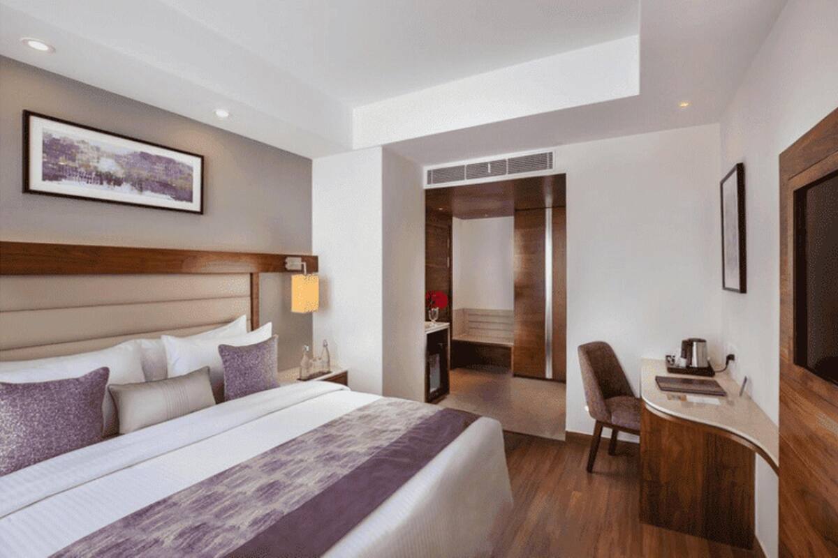 A hotel room with a large bed, a desk, a chair, and a bathroom visible through an open door.
