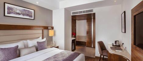 A hotel room with a large bed, a desk, a chair, and a bathroom visible through an open door.