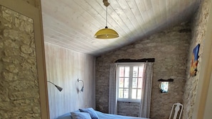 Une chambre à coucher avec un lit, deux chaises, une fenêtre et un mur en pierre.