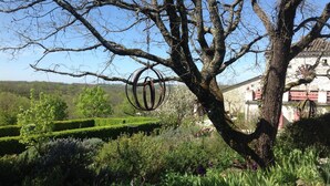 Un arbre orné d’anneaux métalliques, un bâtiment en pierre et un jardin bien entretenu.