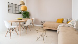 A modern living room with a sofa, a dining table with chairs, and a hanging light fixture.