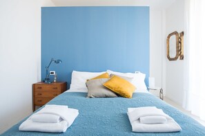 A neatly made bed with blue bedding, two white towels, and two pillows in yellow and gray. - Appartamento Galliera (Bologna)
