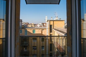 A view from a window with a metal railing, overlooking a cityscape with buildings of various heights and architectural styles. - Appartamento Galliera (Bologna)