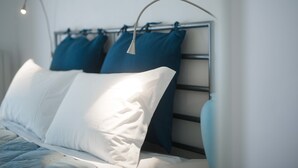 A neatly made bed with white and blue pillows, a metal headboard, and a bedside lamp. - Appartamento Santa Margherita (Bologna)
