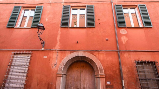 A building with three windows with green shutters, a large wooden door, and a metal grid window. - Appartamento Santa Margherita (Bologna)