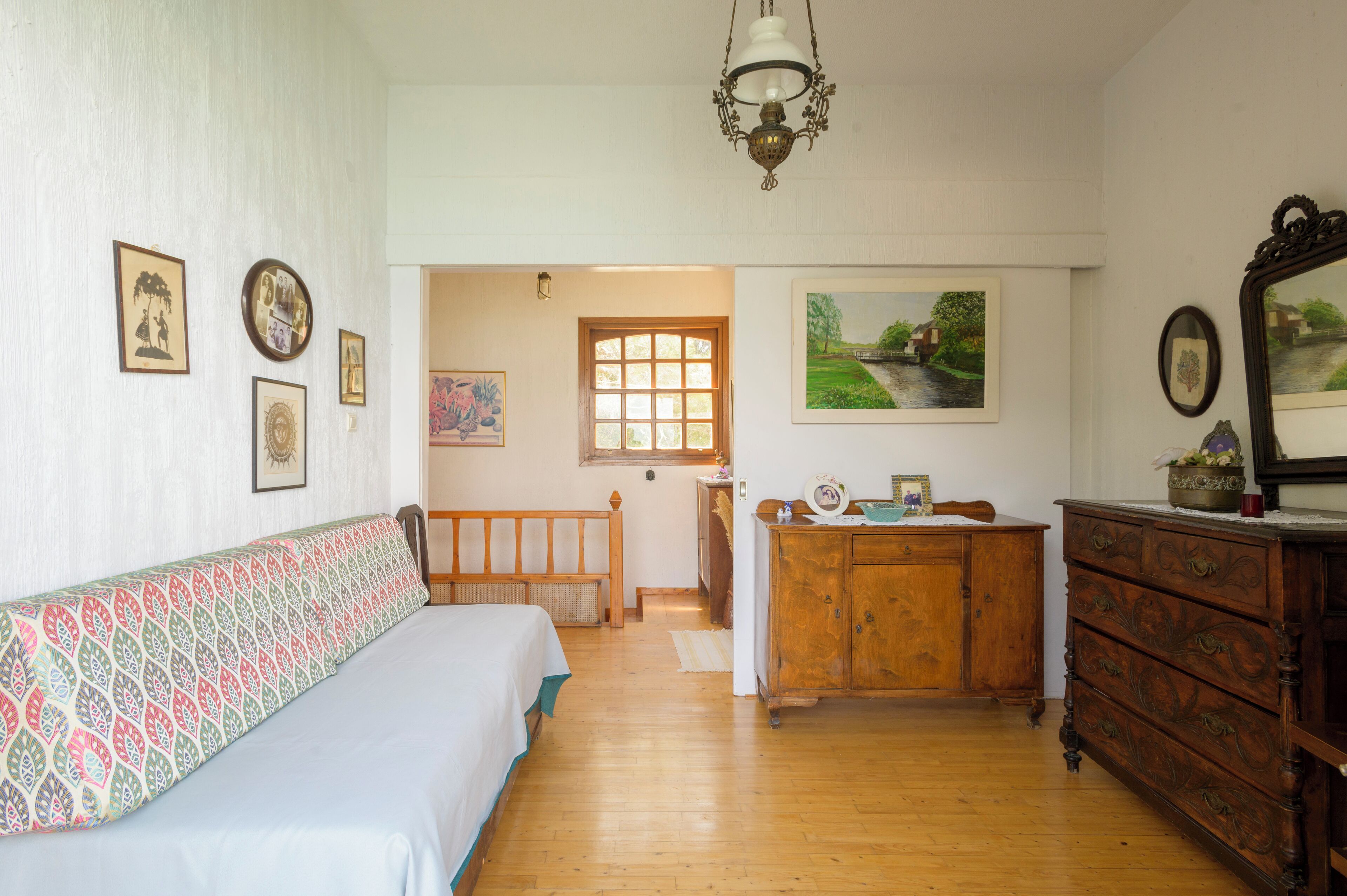 A room with a bed, wooden dresser, and a door leading to another room.