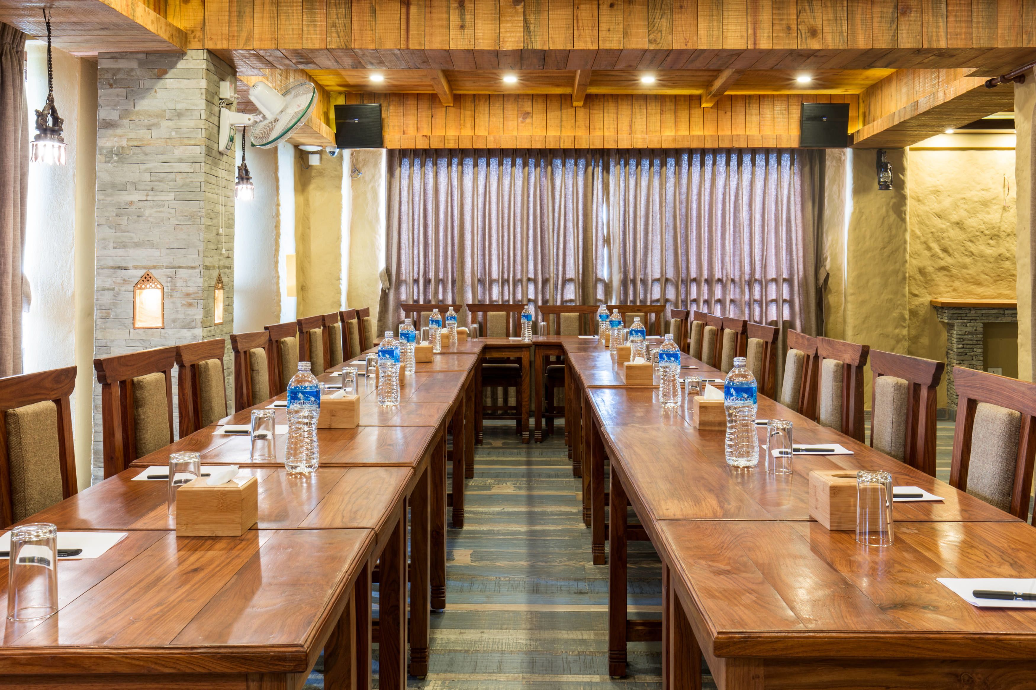 Une salle de conférence avec de longues tables en bois, des chaises, des bouteilles d’eau et de la verrerie.