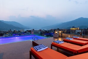 A rooftop pool with lounge chairs and a view of mountains.