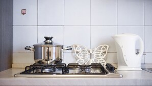 Une cuisine équipée d’une cuisinière à gaz, avec une casserole sur le feu, une bouilloire blanche et un élément décoratif en forme de papillon accroché au mur.