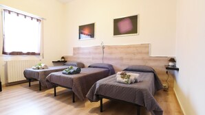 Une chambre d’hôtel avec trois lits simples, une tête de lit en bois, une fenêtre avec des rideaux et deux œuvres d’art accrochées au mur.