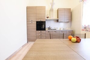 A modern kitchen with wooden cabinets, a dining table, and a fruit bowl with oranges and apples.