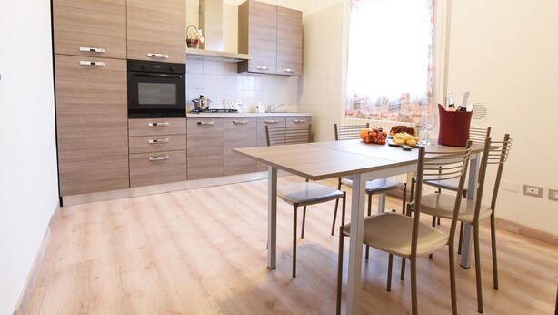 Une cuisine moderne avec des meubles en bois, un four encastré et un coin repas comprenant une table et des chaises.
