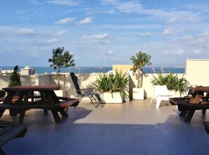 A rooftop terrace with picnic tables, potted plants, and a view of the sea. - G38 Rental Apartment Building (Haifa)