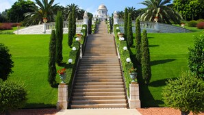 Un grand escalier menant à un bâtiment surmonté d’un dôme, entouré de jardins soignés et de palmiers.
