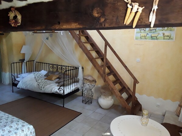Un dormitorio con cama, una escalera de madera, un jarrón blanco y un cuadro de ovejas en la pared.