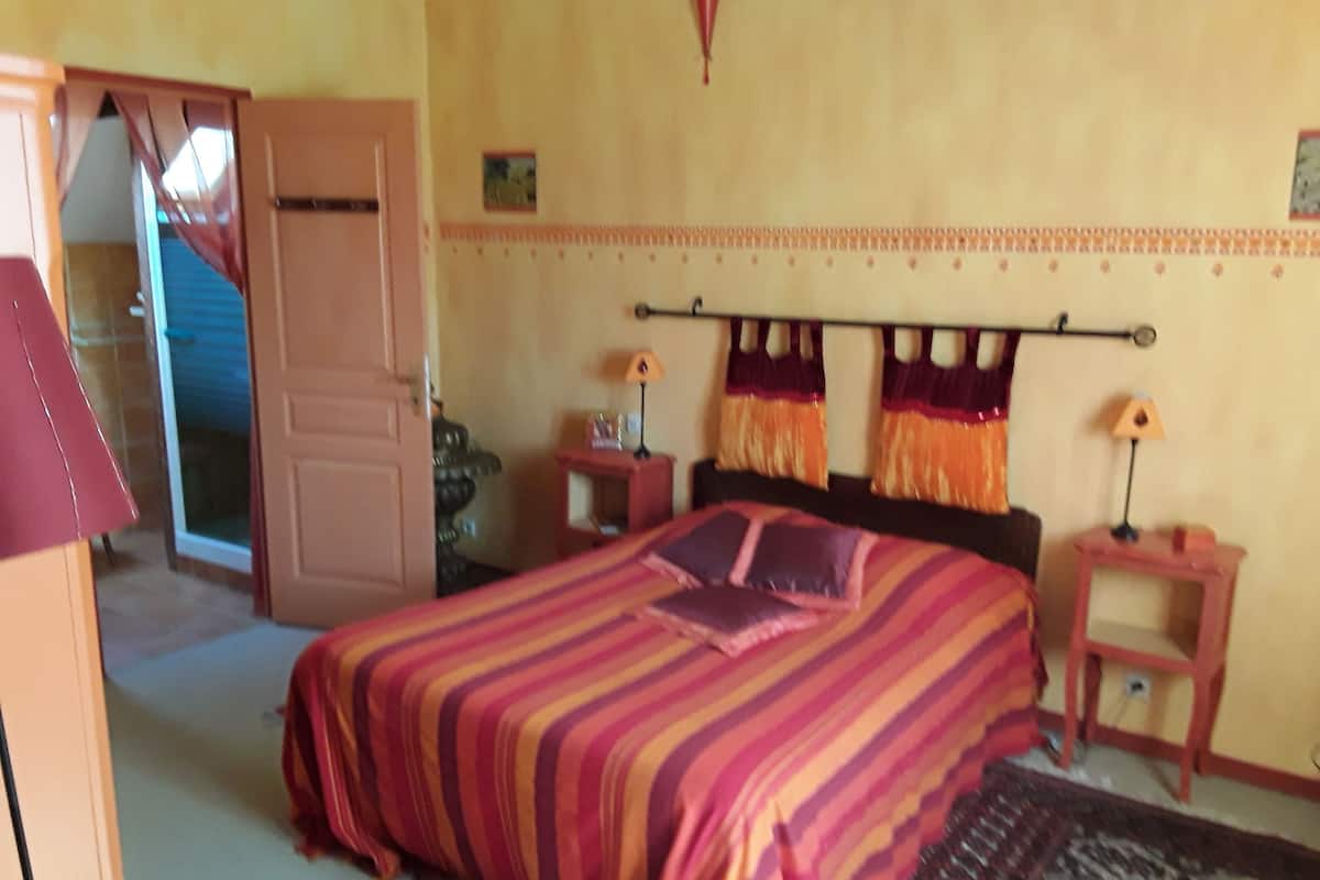 Een slaapkamer met een bed, nachtkastje, lamp, deur en trap.
