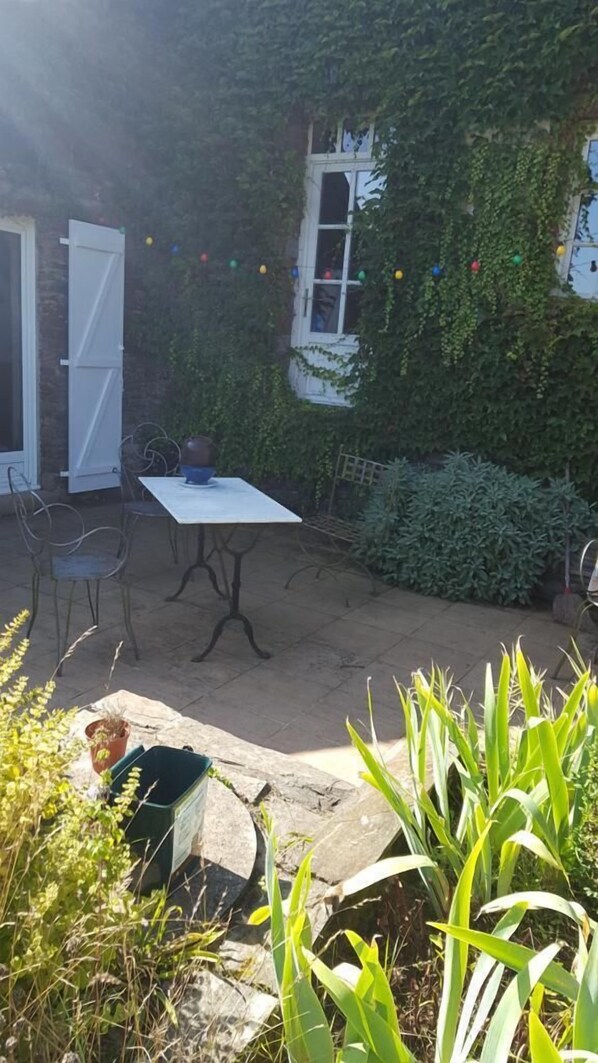 A patio area with a table and chairs, surrounded by greenery and a white door. - Chambres d'hotes la Merais (Marsac-sur-Don)