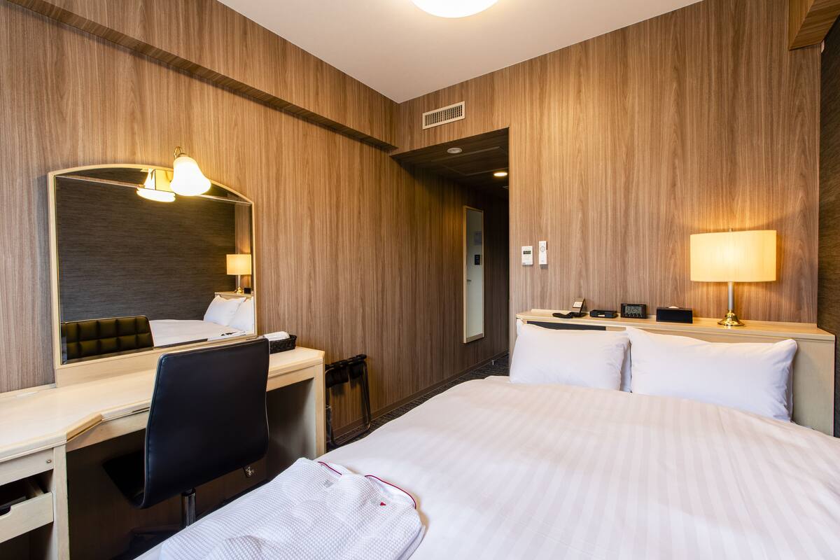 A hotel room with a bed, desk, chair, and a large mirror.