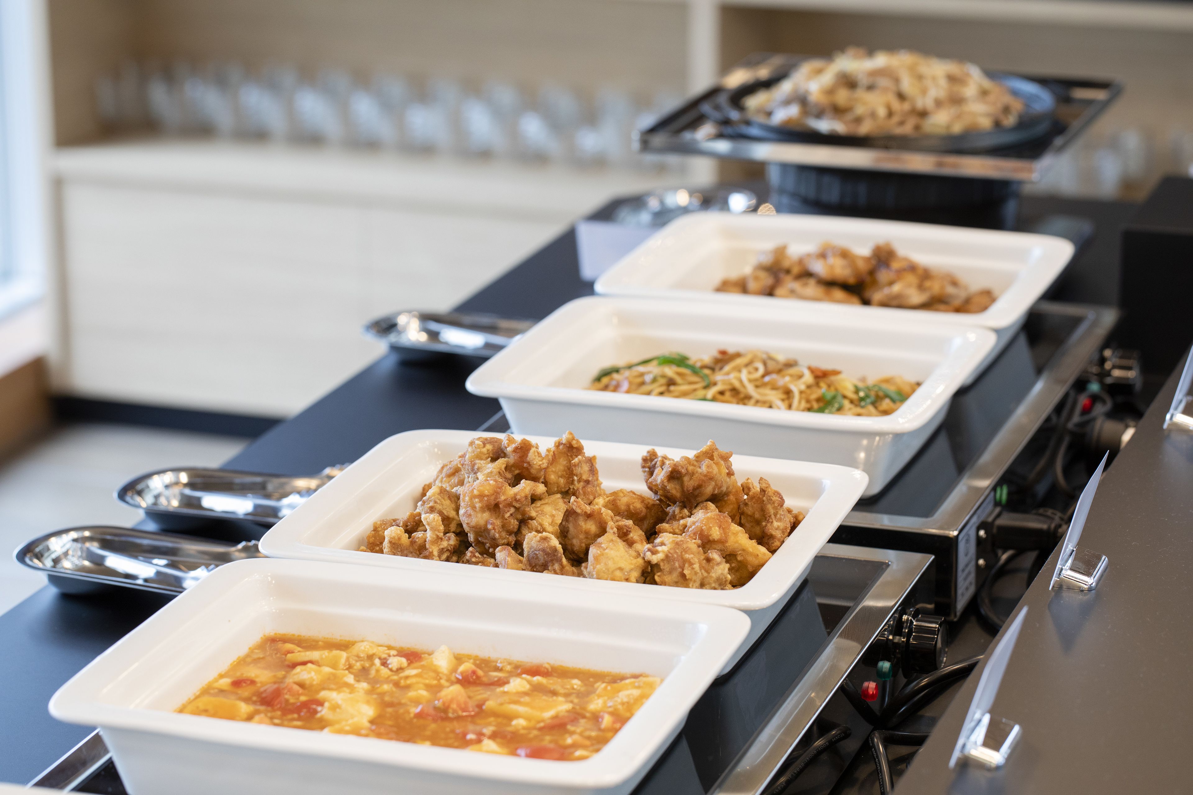 A buffet with various dishes including fried chicken, noodles, and a soup.