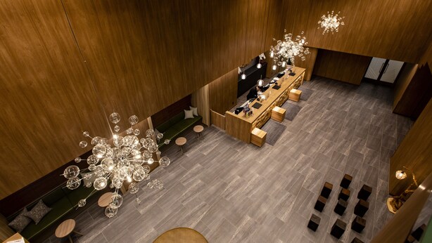 A modern hotel lobby with a wooden reception desk, seating area, and a chandelier.