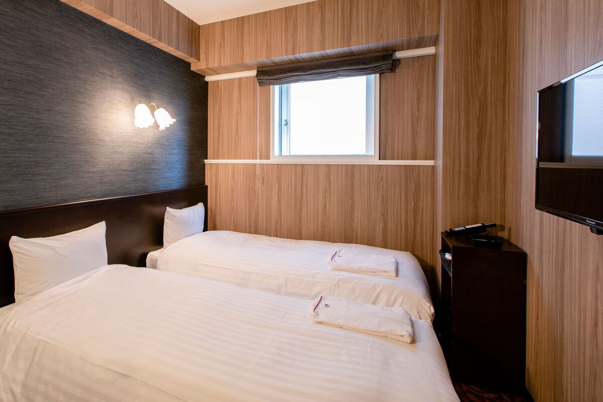 A hotel room with two beds, a TV, and a window with a view.