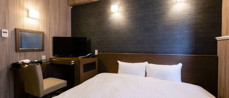 A hotel room with a bed, a desk with a television, a chair, and a wall-mounted light.