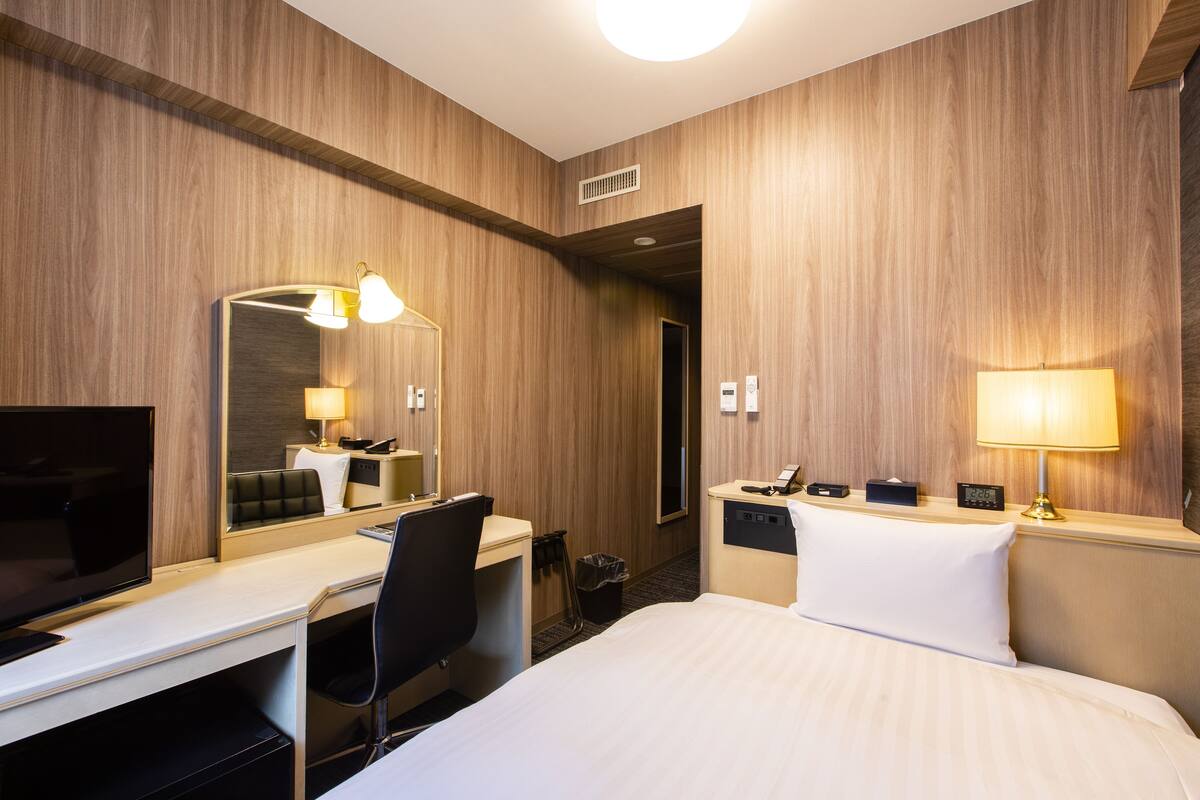 A hotel room with a bed, desk, chair, television, and two bedside lamps.