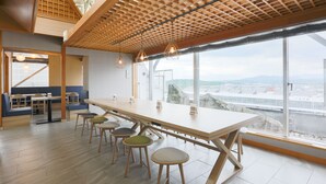 A modern interior with a long table and stools, large windows, and a view of the city.