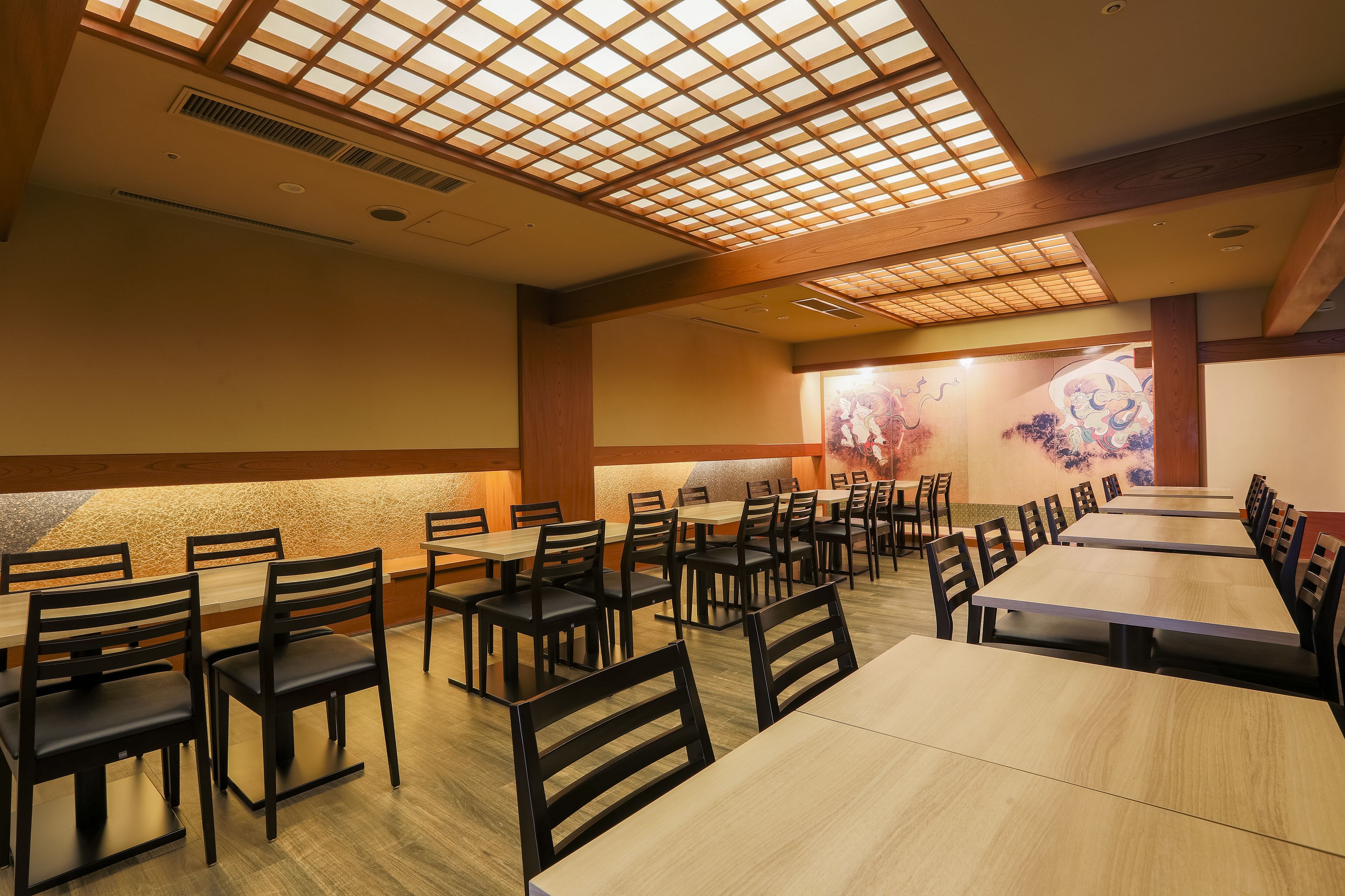 Un restaurante con mesas y sillas de madera, un techo alto con entramado de madera y un mural en la pared del fondo.