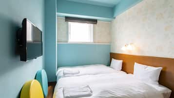 A hotel room with a bed, a television, a window with a curtain, and a wall with floral wallpaper.