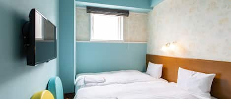 A hotel room with a bed, a television, a window with a curtain, and a wall with floral wallpaper.