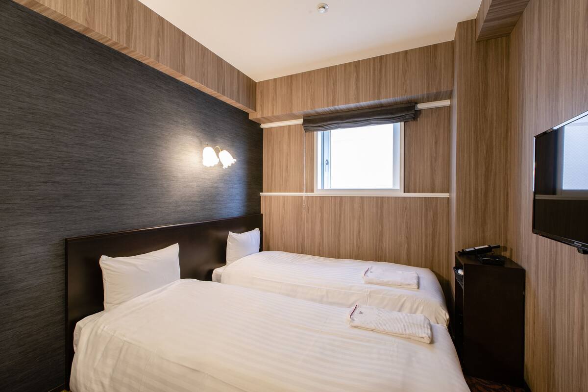 A hotel room with two beds, a TV, and a window with a view.