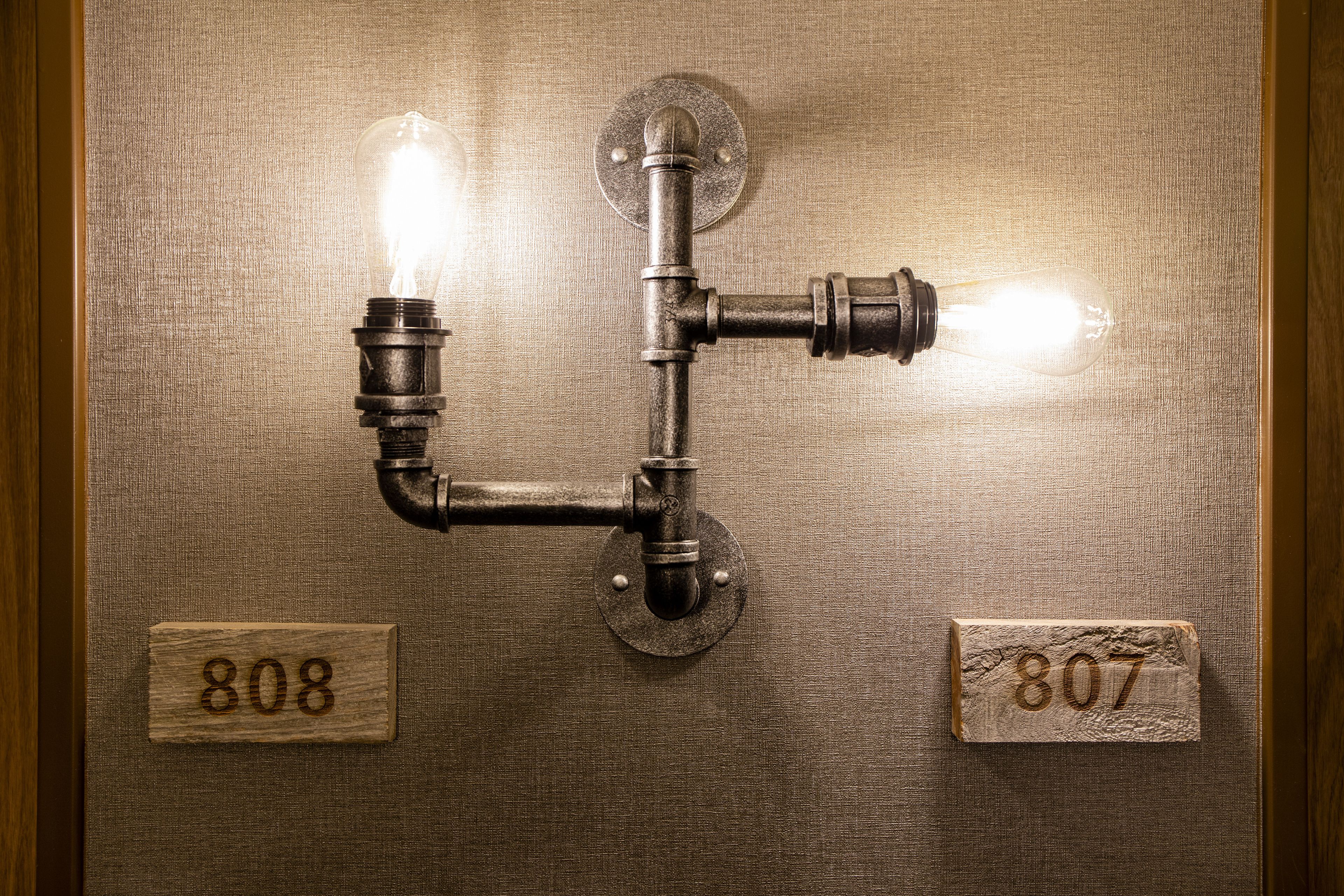 Una lámpara de pared con dos bombillas a la vista y dos placas de madera con los números "808" y "807".