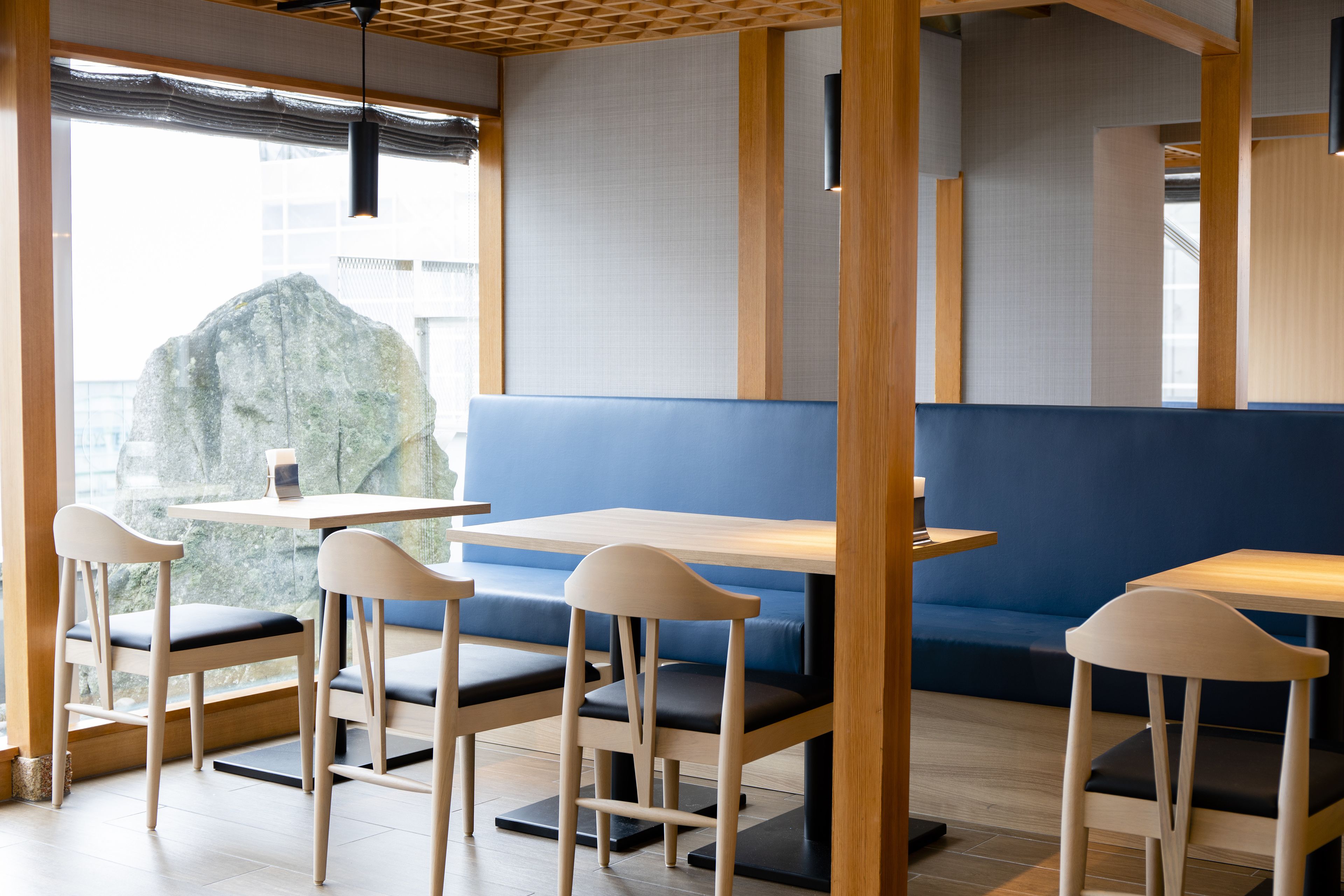 Ein modernes Restaurant mit Holztischen, blauen Sitzplätzen und einer großen Felsdekoration.
