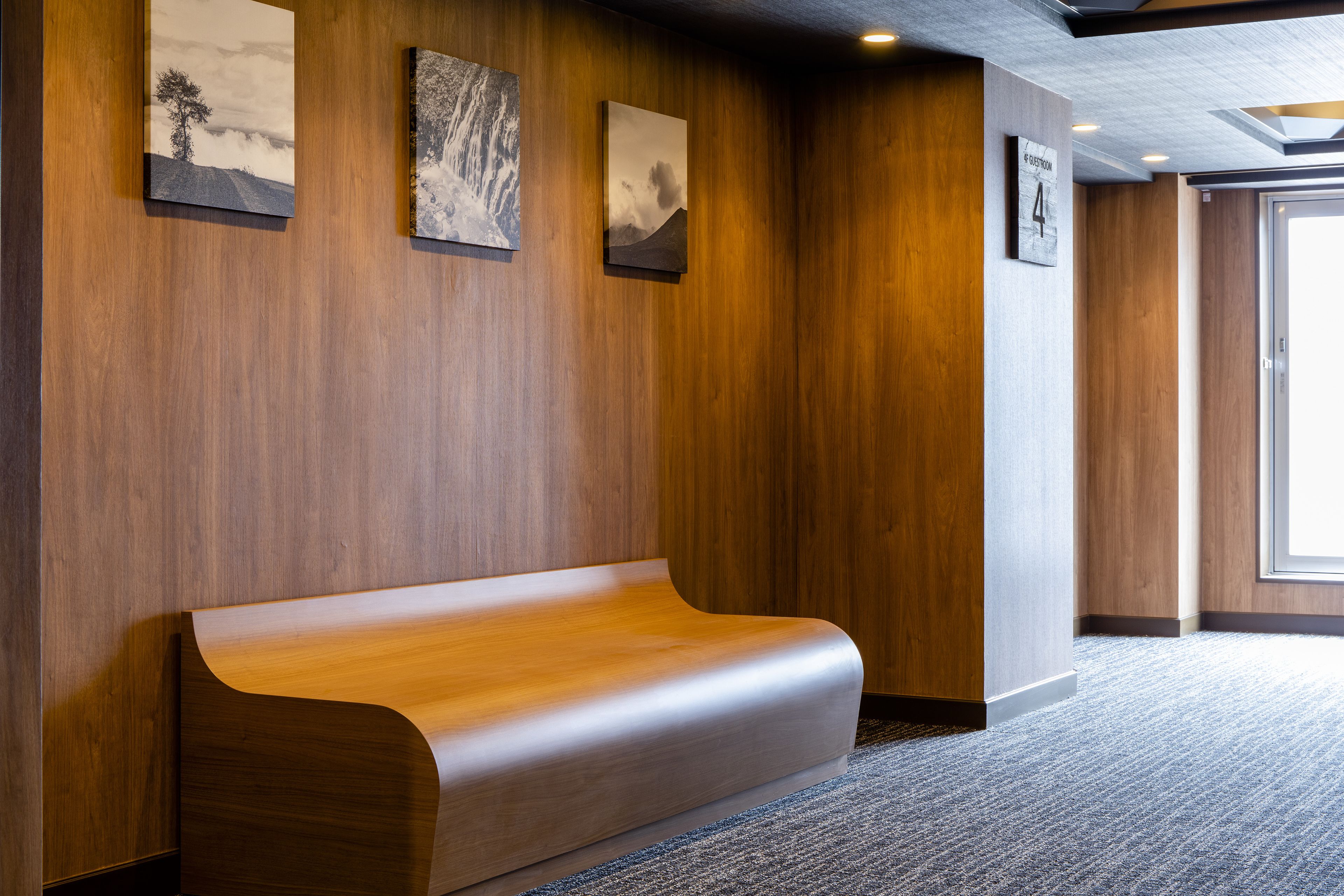 Un hall d’entrée moderne avec un banc en bois, des œuvres d’art encadrées accrochées aux murs et un sol recouvert de moquette.