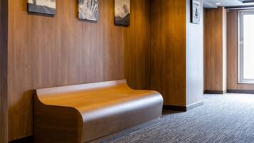 A modern lobby with a wooden bench, framed artwork on the walls, and a carpeted floor.