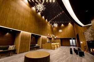 Un hall d’entrée spacieux avec des lambris en bois, un comptoir d’accueil, des coins salon et une grande table ronde.