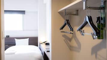Una habitación de hotel con cama, mesita de noche y perchero con perchas.