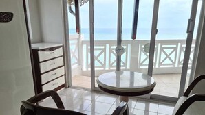 A balcony with a table and chairs, a white cabinet, and a view of the sea. - Le Recif Guest House (Rodrigues Island)
