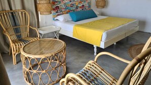A room with a bed, two wicker chairs, a small table, and a colorful wall art piece. - Le Recif Guest House (Rodrigues Island)