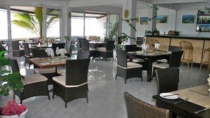 A restaurant with wicker furniture, glass tables, and a bar area. - Le Recif Guest House (Rodrigues Island)