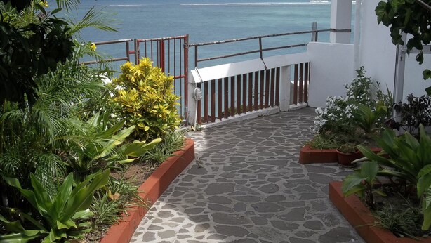 A stone pathway leading to a balcony with a view of the ocean. - Le Recif Guest House (Rodrigues Island)