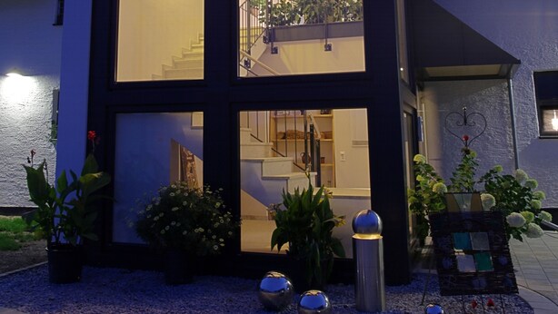 Una casa moderna con un amplio ventanal, una escalera y un balcón con plantas.