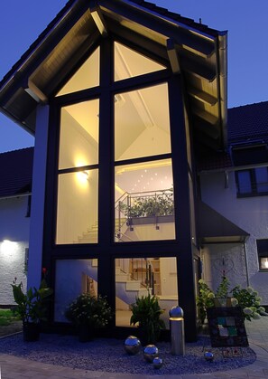 A modern house with a large glass window, a staircase, and a balcony with plants.