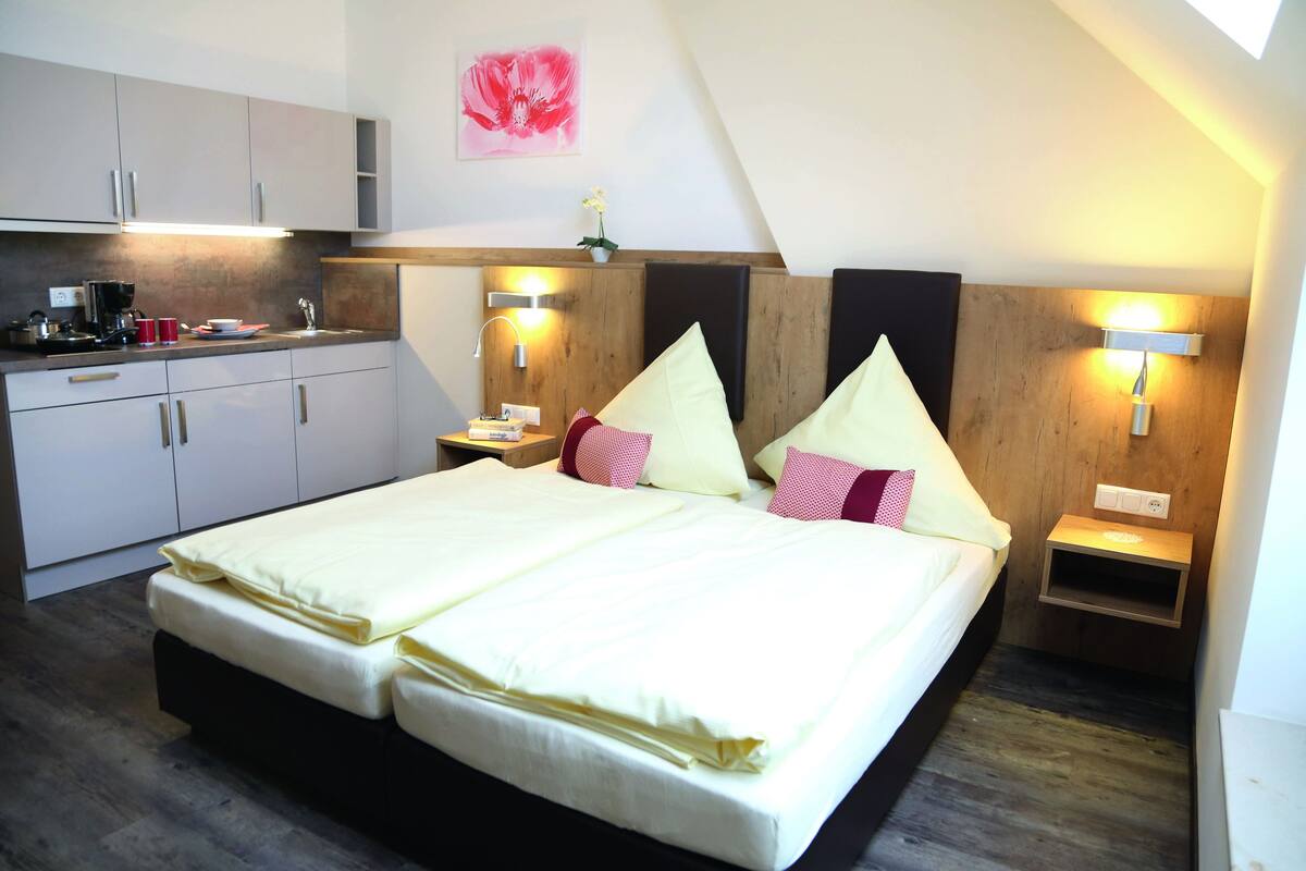 A bedroom with a double bed, a small kitchenette, and two bedside tables with lamps.