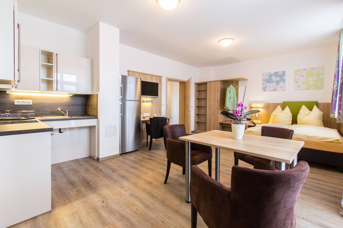 A modern kitchen with a dining area, a sofa, and a bed in a well-lit room.