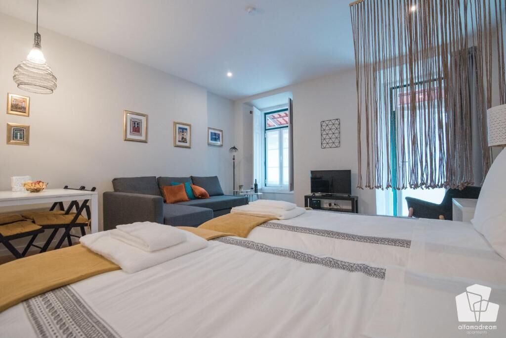 A hotel room with two beds, a desk, a chair, a TV, and a large window with curtains.