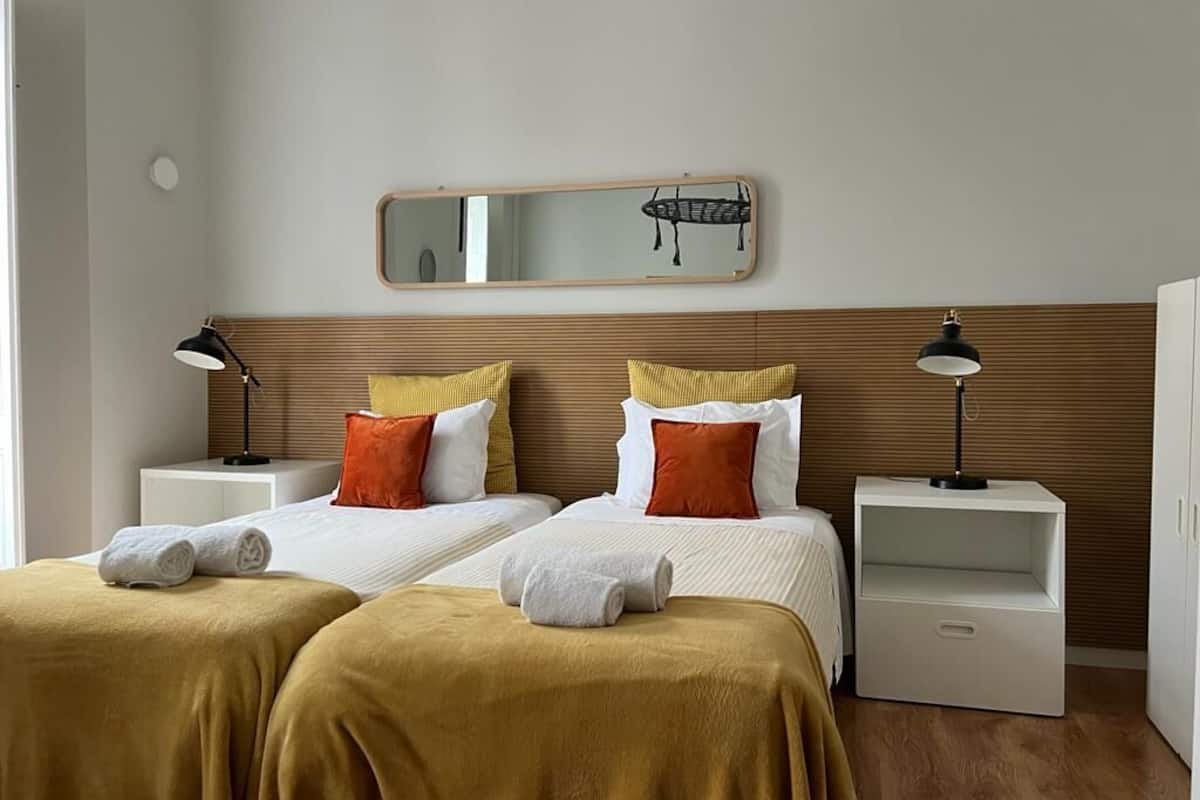 Een hotelkamer met twee bedden, een houten hoofdbord, een spiegel, bedlampjes en een klein wit kastje.